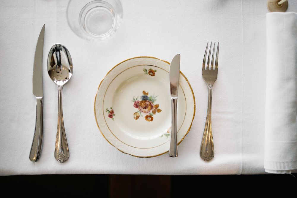 Formal place setting with vintage floral plate and silverware on white tablecloth.