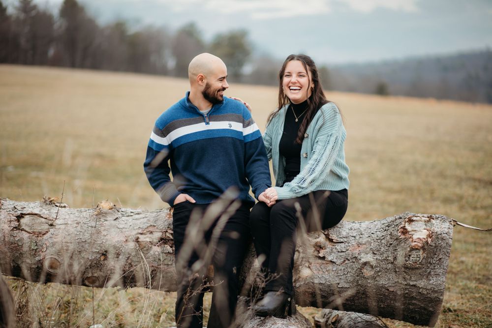 Couple sits together on fallen tree trunk in scenic outdoor setting.