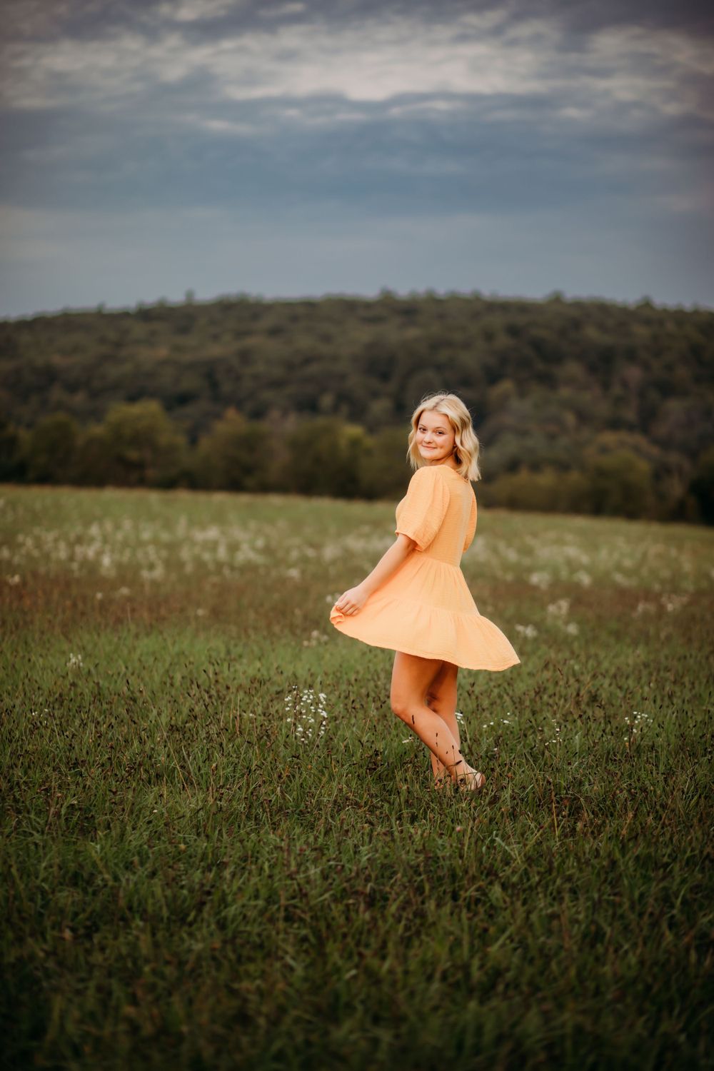 Person in flowing orange dress twirls in meadow during outdoor photoshoot.
