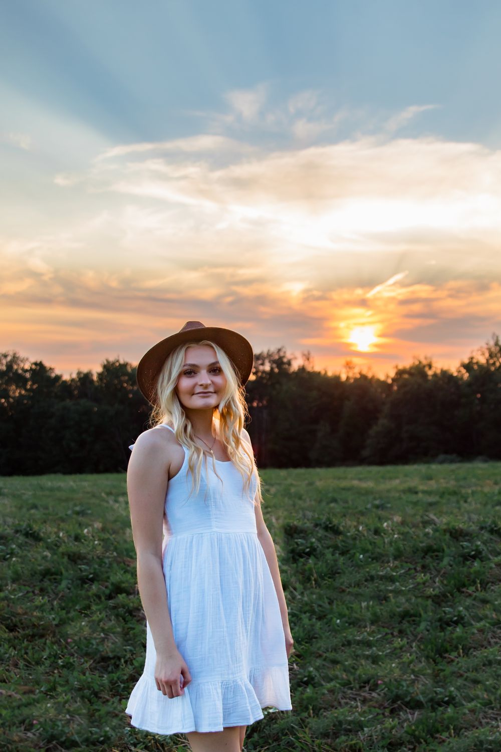 Person in white dress poses against sunset sky during golden hour photoshoot.