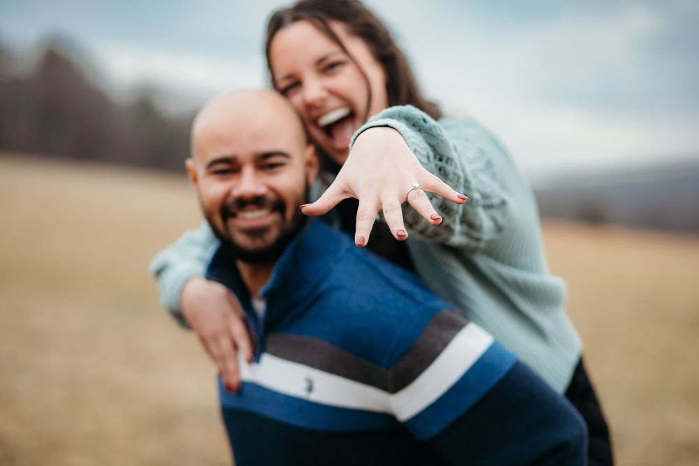Couple sharing candid laughter while sitting on log in rustic outdoor setting.
