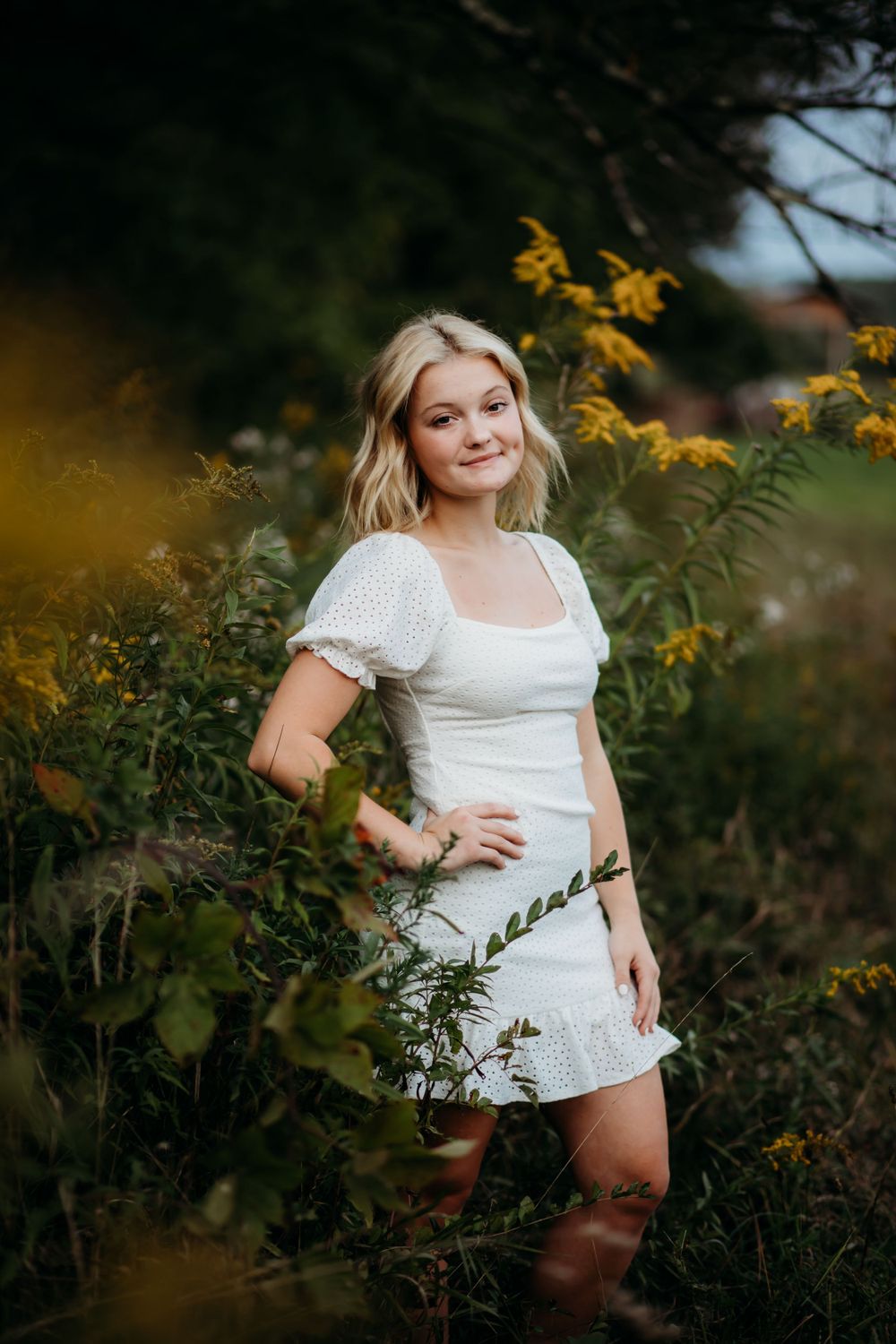 Person in white dress poses among wildflowers during outdoor portrait session.