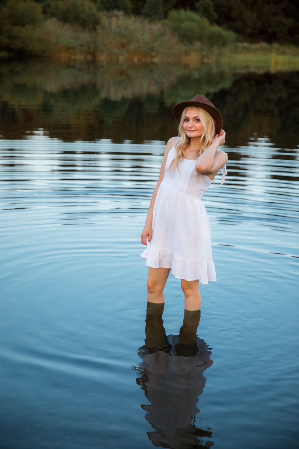 Artistic photo sequence of someone wading in calm lake water wearing a flowing white dress.