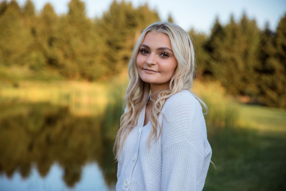 Person in light colored sweater smiles during outdoor autumn photoshoot.