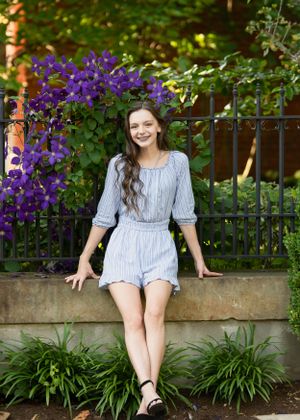Summer portrait against iron fence with purple clematis flowers blooming in background.  Senior Photographer Batavia Cincinnati Ohio