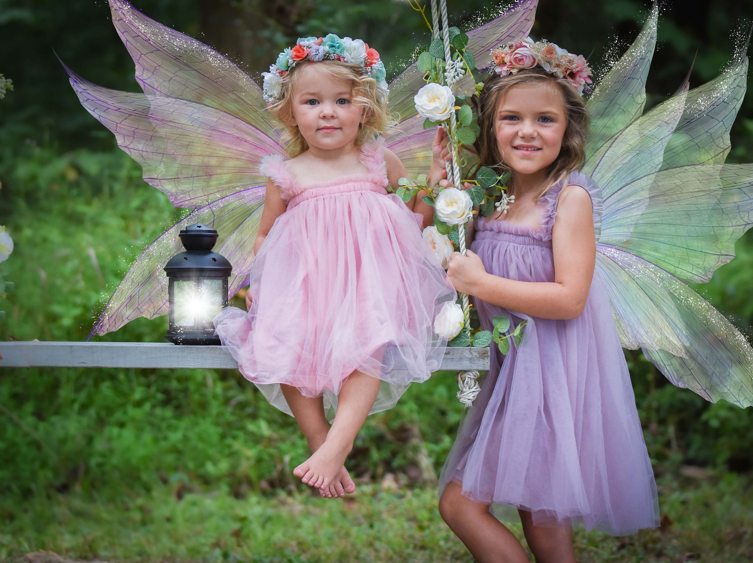 Two fairy-costumed children pose with glittery wings and lanterns in a magical garden setting. Family Dance photographer Batavia Cincinnati