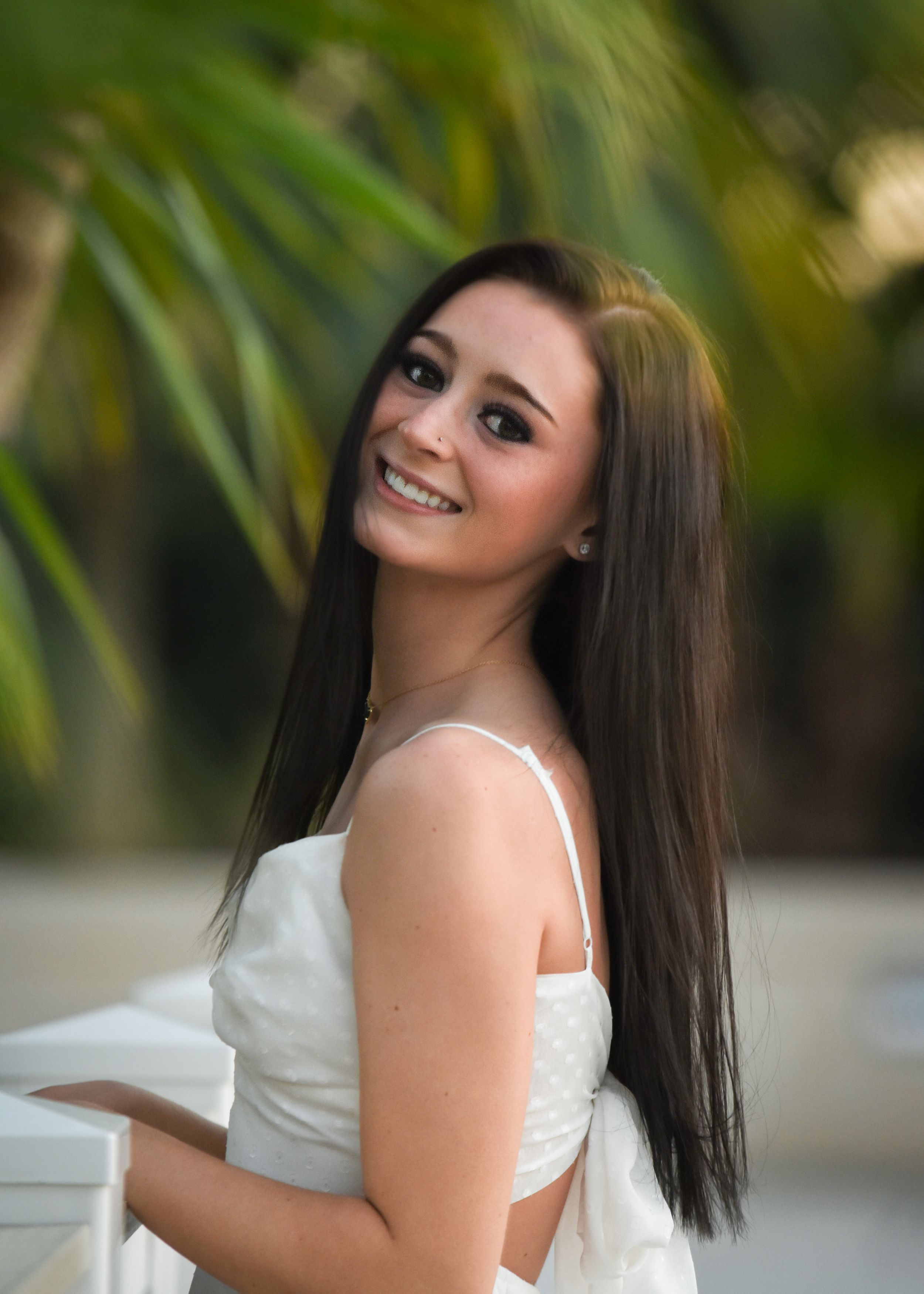 Portrait of woman in white dress smiling against tropical palm background. Senior photographer Batavia Cincinnati Ohio