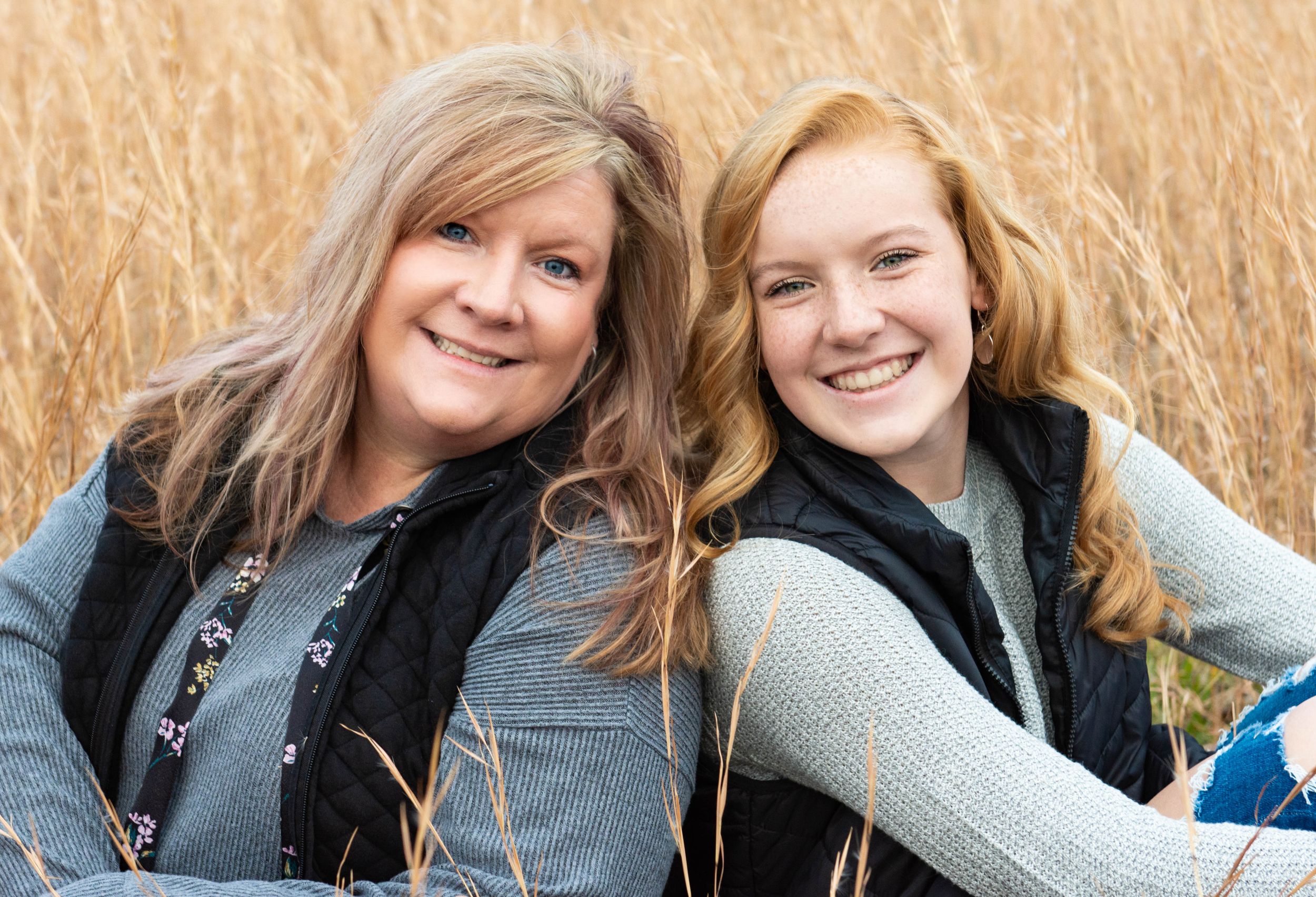 Two people sitting together and smiling in a golden wheat field on a sunny day. Family Photographer Batavia Cincinnati Ohio