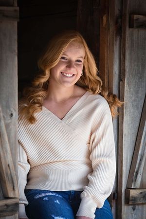 Portrait of person in cream sweater sitting in rustic barn doorway. Senior Photographer Batavia Cincinnati Ohio