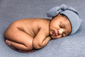 Posed newborn photo of little boy in hat on blue backdrop