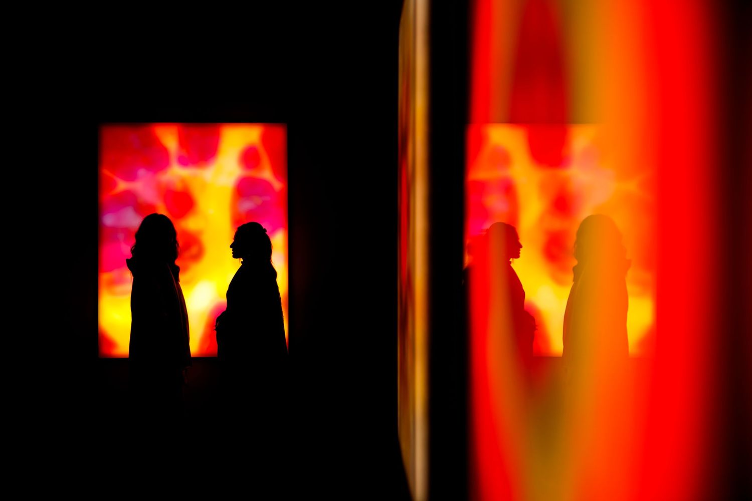Silhouettes of two figures against vibrant red and orange backlit display.