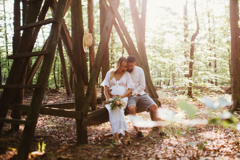 Couple sitting together under wooden structure in sunlit autumn forest.