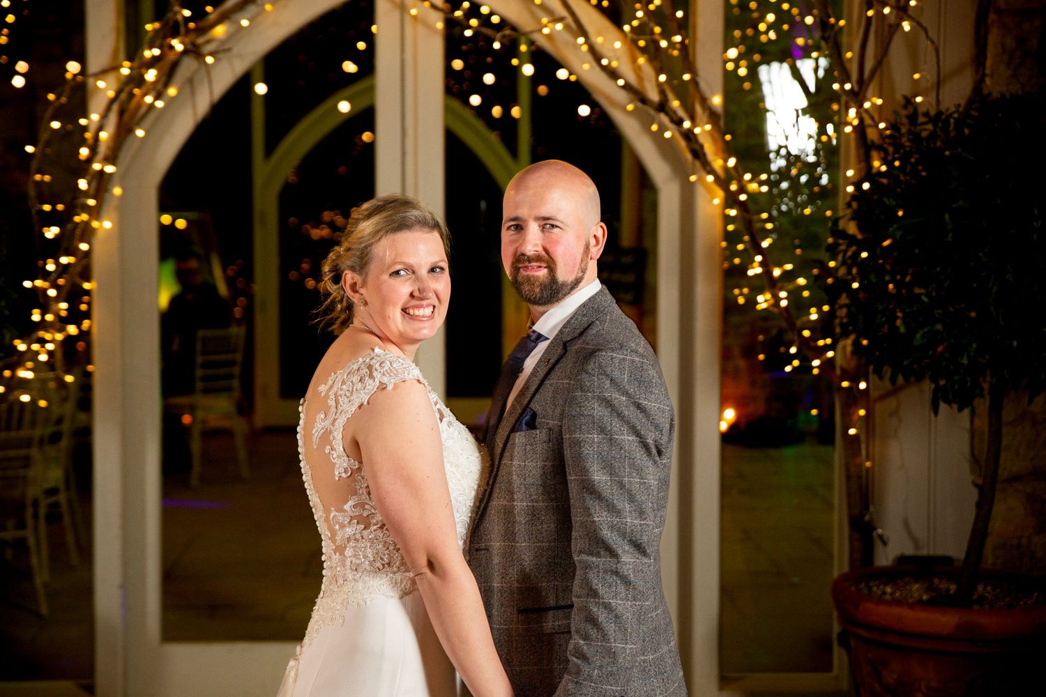 Wedding couple dancing under string lights at an elegant evening reception.