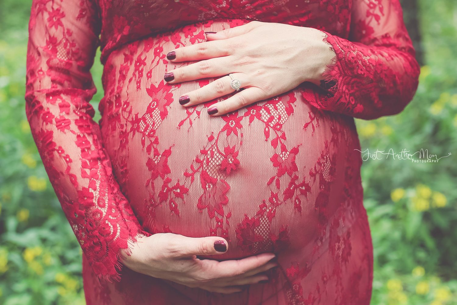 A close-up of hands cradling a pregnant belly through red lace maternity dress.