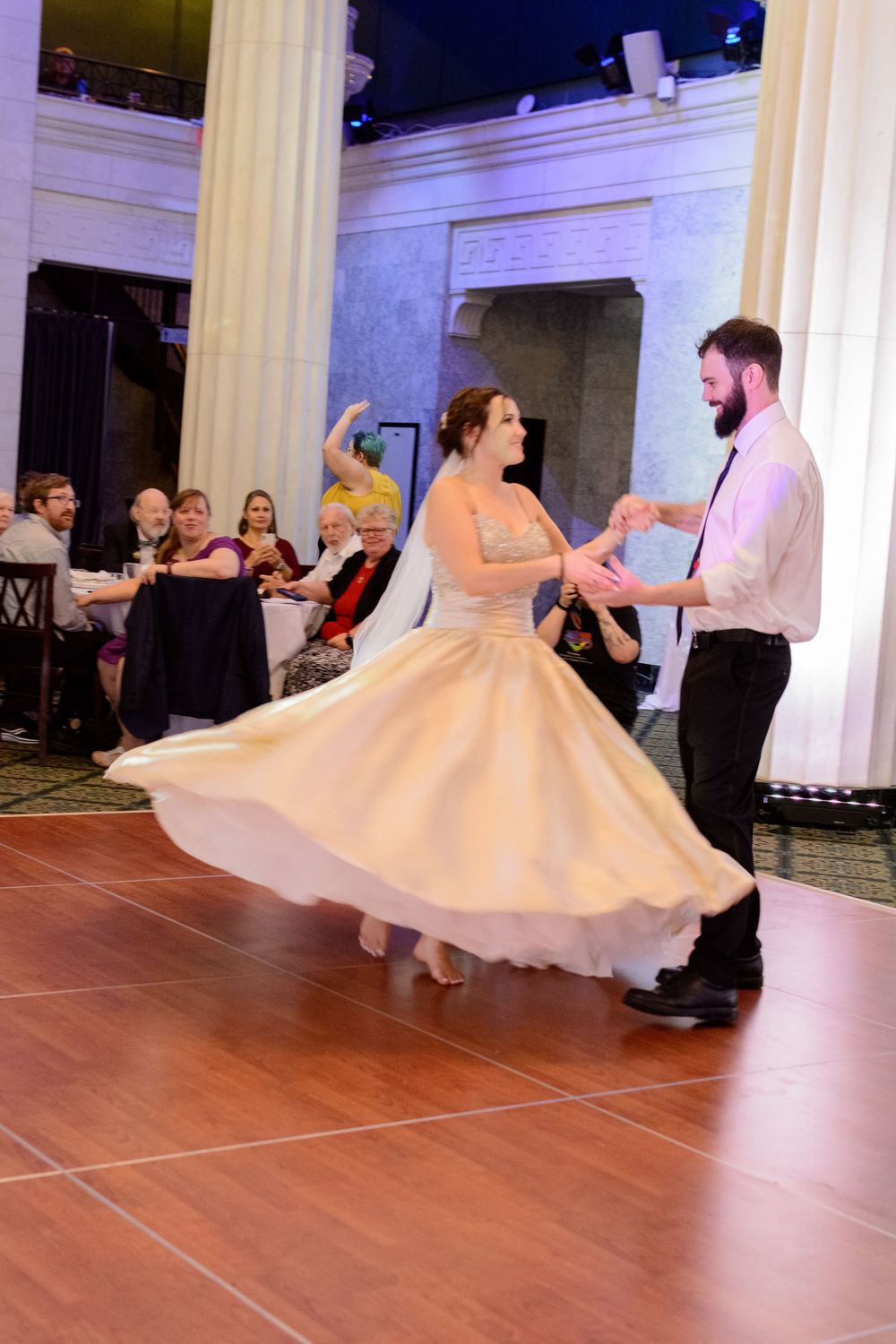 A dancing couple twirls on the hardwood floor at an elegant wedding reception.
