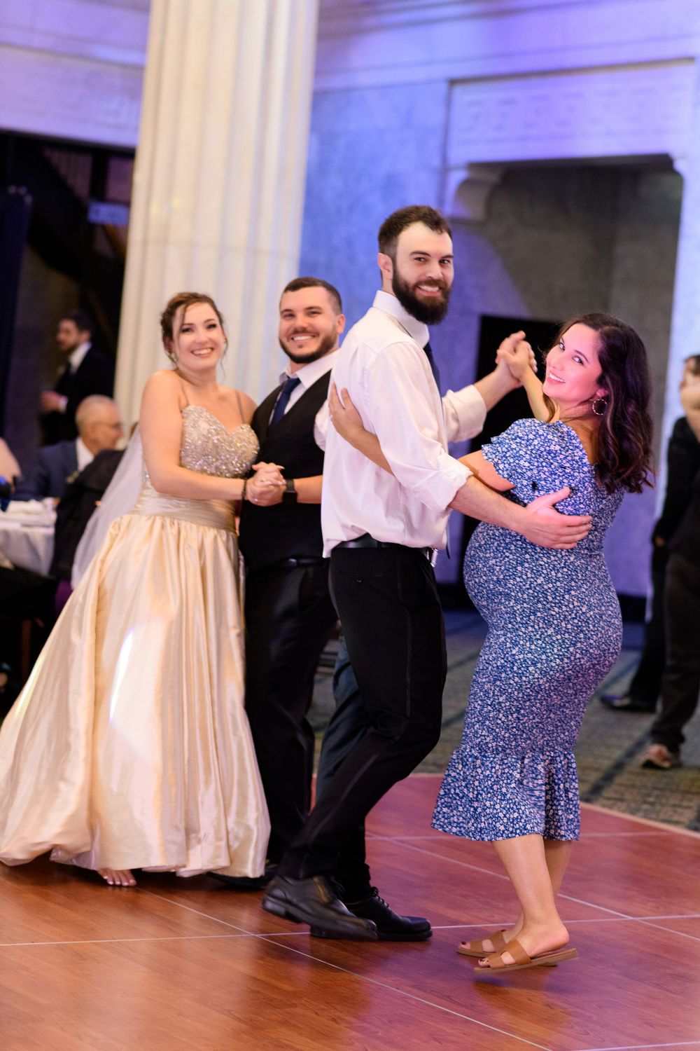 Couples dancing in formal attire at a wedding reception with elegant white columns and decor.