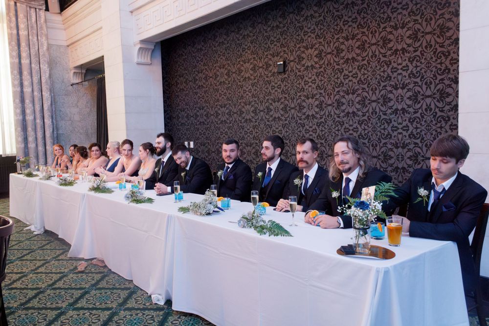 Long head table at formal event with elegant place settings and floral centerpieces.