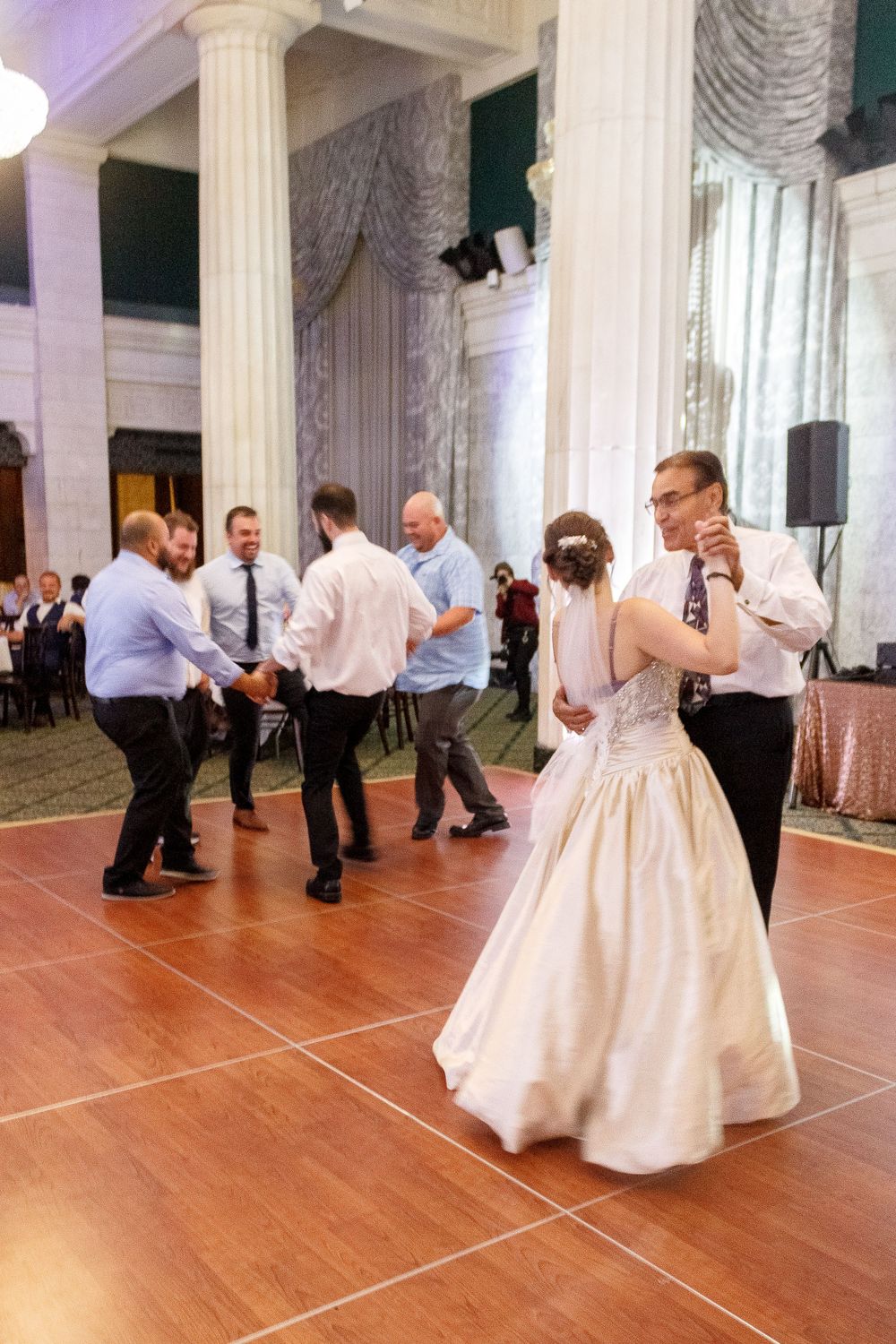 Wedding guests dancing on a wooden floor surrounded by classical white columns and elegant decor.