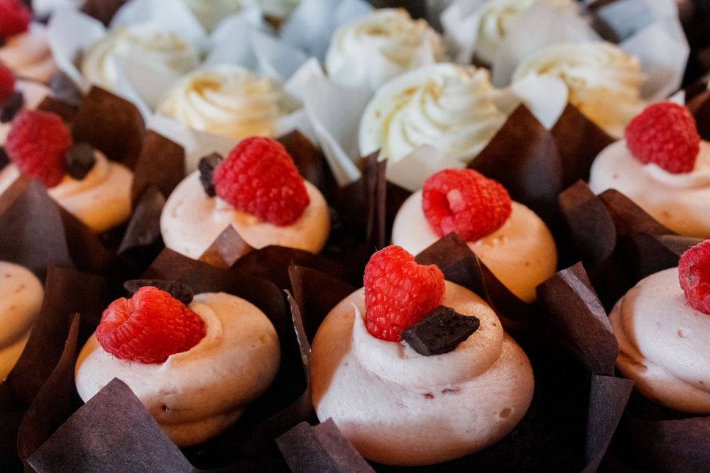 Mini dessert cups topped with fresh raspberries and chocolate garnish arranged in brown paper holders.