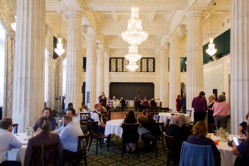 Elegant reception hall with white columns and crystal chandeliers where guests are dining.