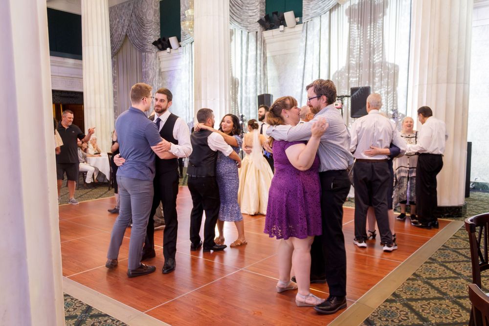 Couples dancing together at an elegant wedding reception on a hardwood dance floor with white pillars and drapes.