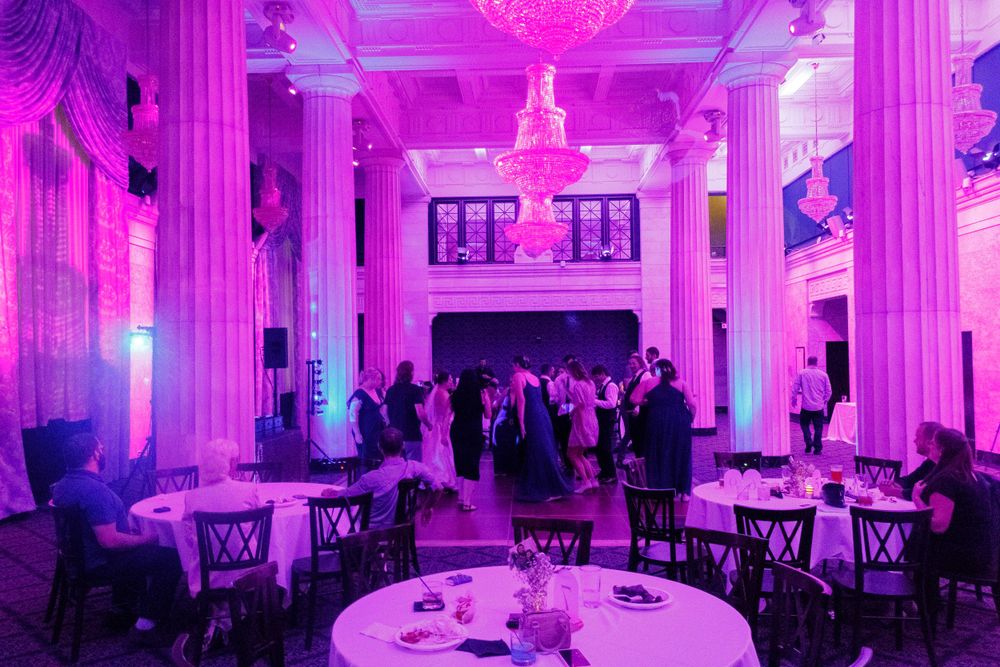 Elegant ballroom bathed in purple lighting with chandelier and round tables for a wedding reception.