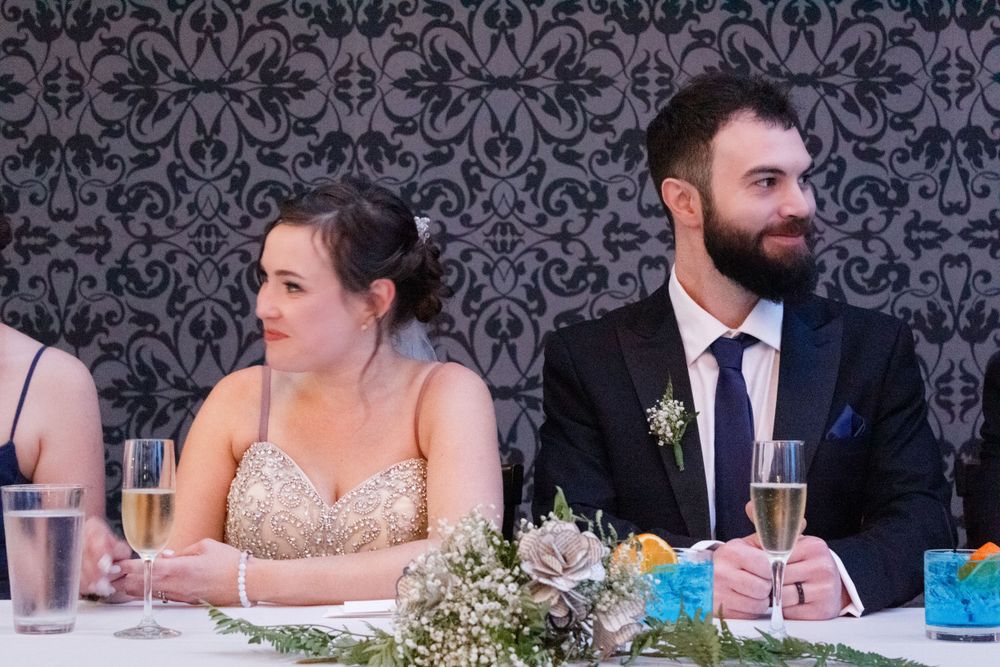 Wedding reception table with floral decorations and damask wallpaper backdrop.