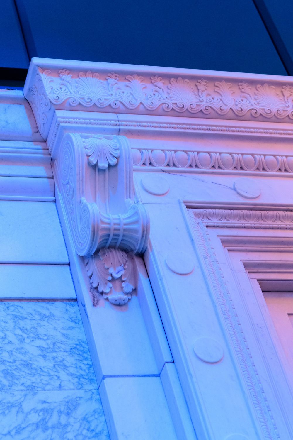 Ornate architectural detail with carved molding illuminated by blue and pink lights.