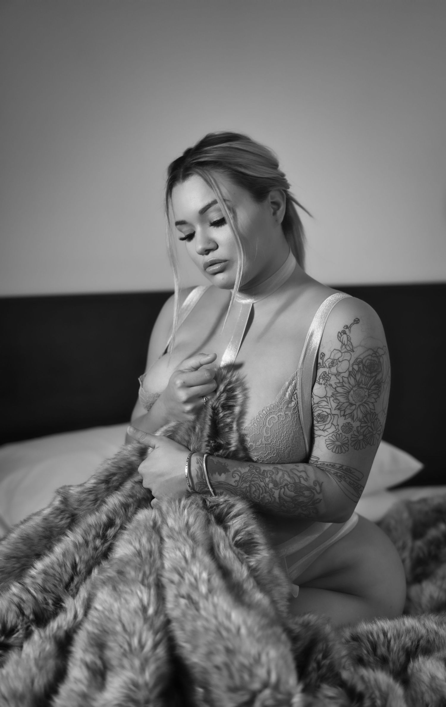 Moody boudoir photograph with a person in lingerie holding a fuzzy blanket in black and white.