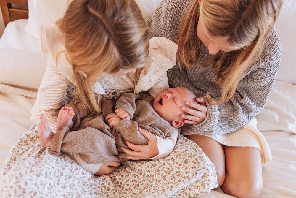 Gentle hands cradling a newborn baby on white bedding.