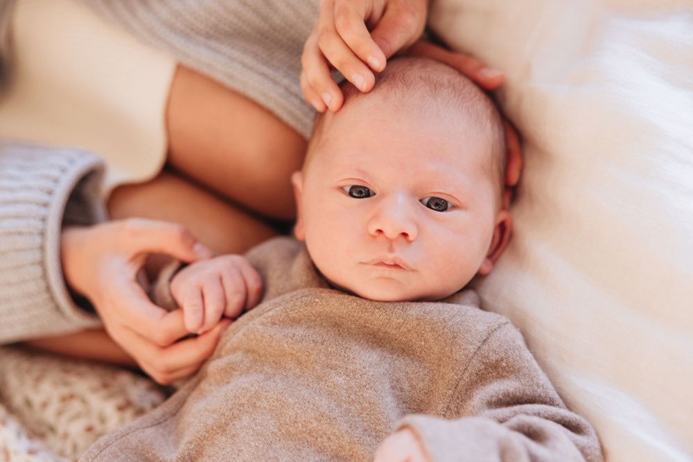 Close-up of a newborn baby in gray clothing lying on white bedding.