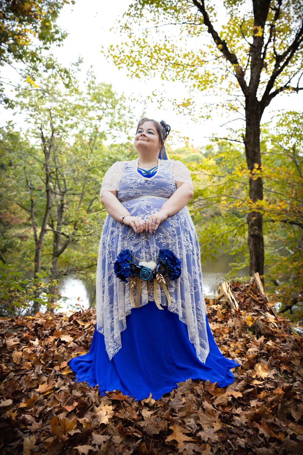 A bride in a blue and white lace gown poses among fallen autumn leaves.