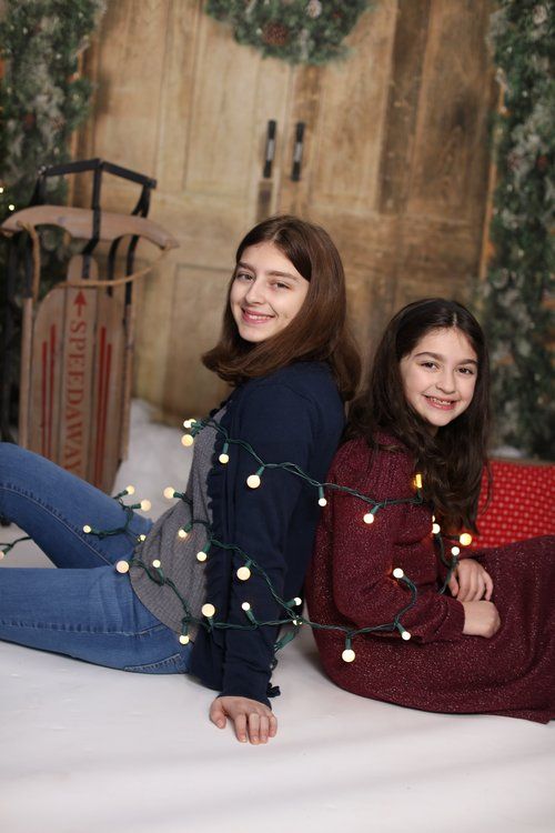 Two people wrapped in Christmas lights posing on floor with holiday decorations.