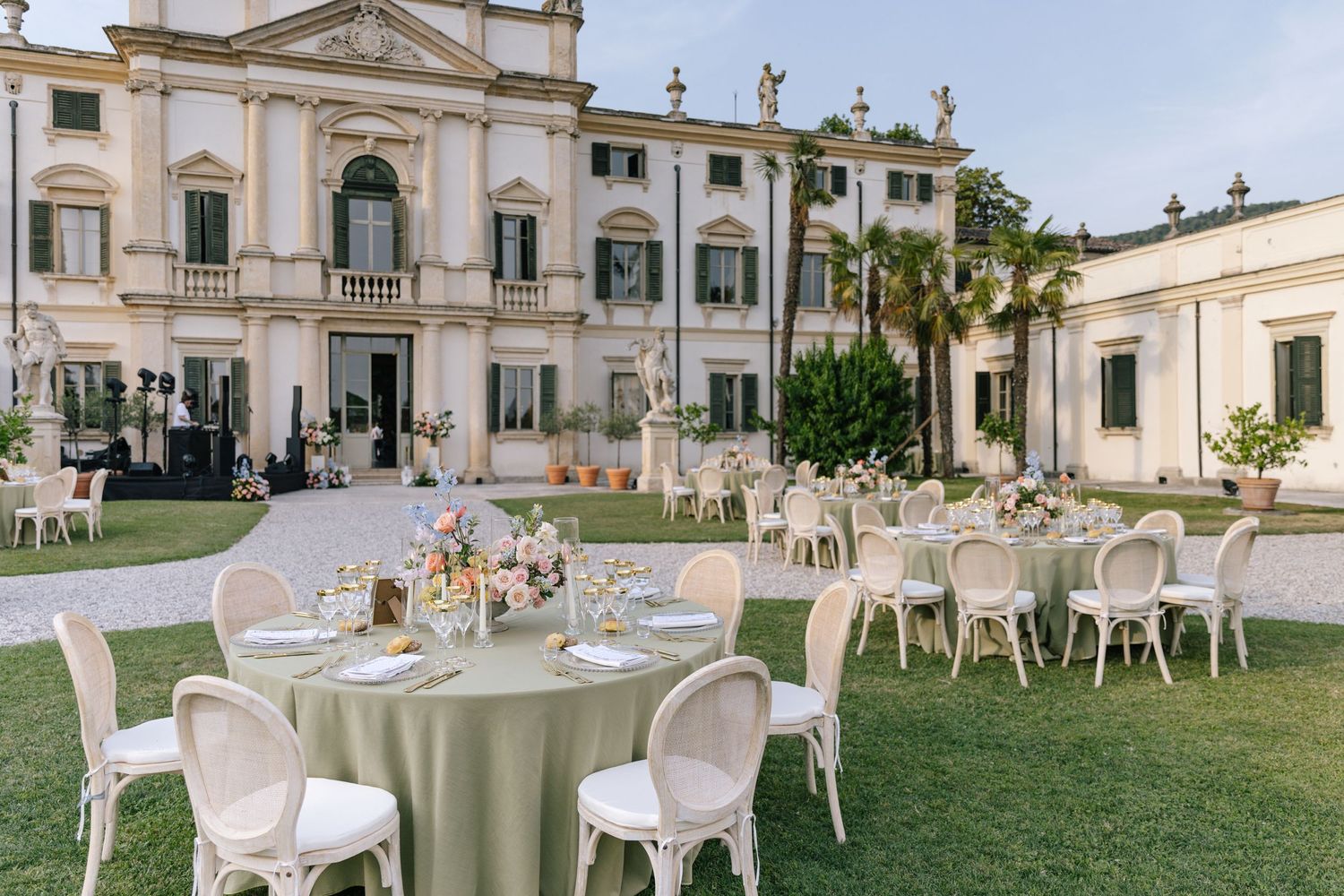 Outdoor wedding reception setup with round tables on the lawn of an elegant Italian villa.