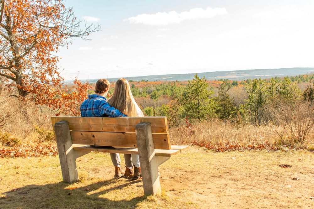A couple enjoys the scenic fall view while sitting together on a wooden bench.