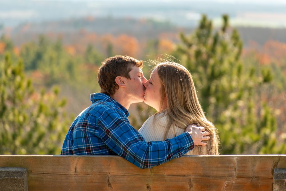 A romantic moment shared between a couple on a wooden bench overlooking autumn scenery.