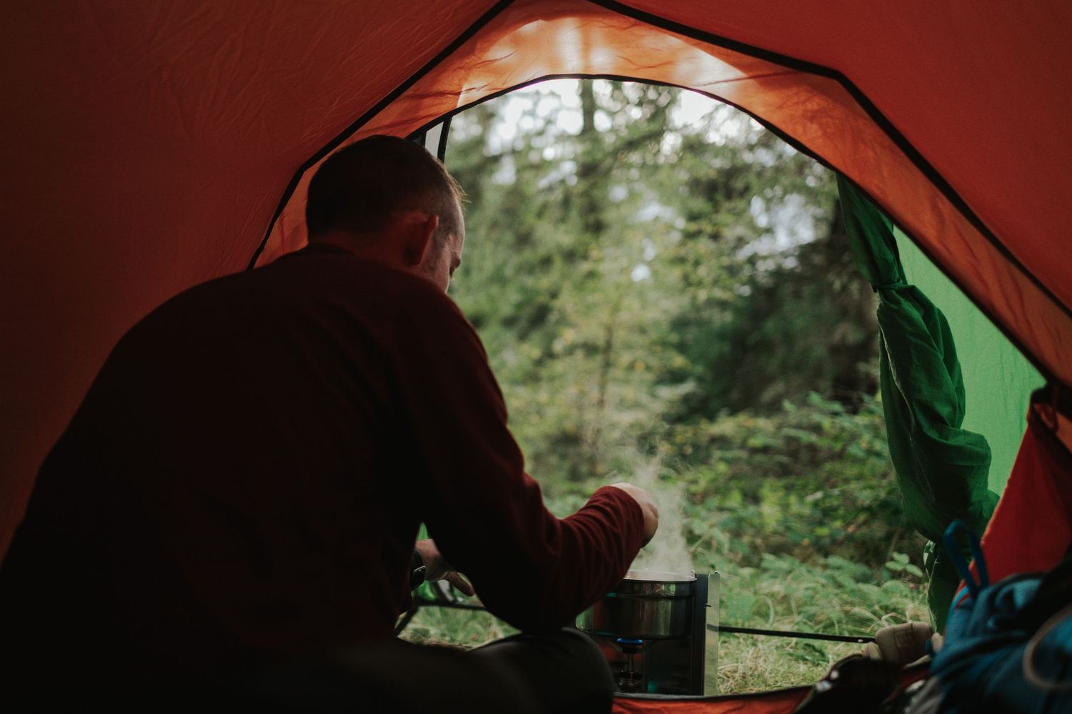 Silhouette inside tent holding coffee mug while camping in forest.