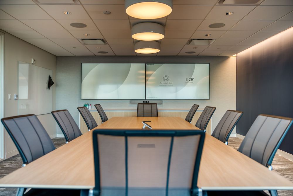 Corporate boardroom with large conference table, gray chairs, and pendant lighting.
