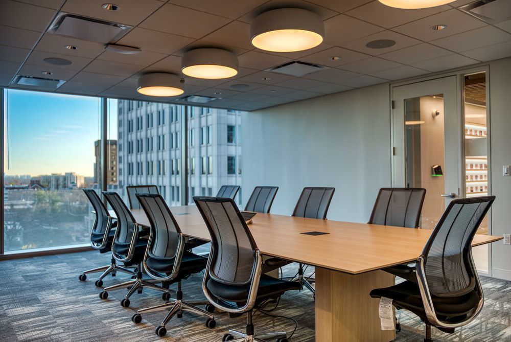 Modern conference room with wooden table, mesh office chairs, and large windows overlooking city skyline.
