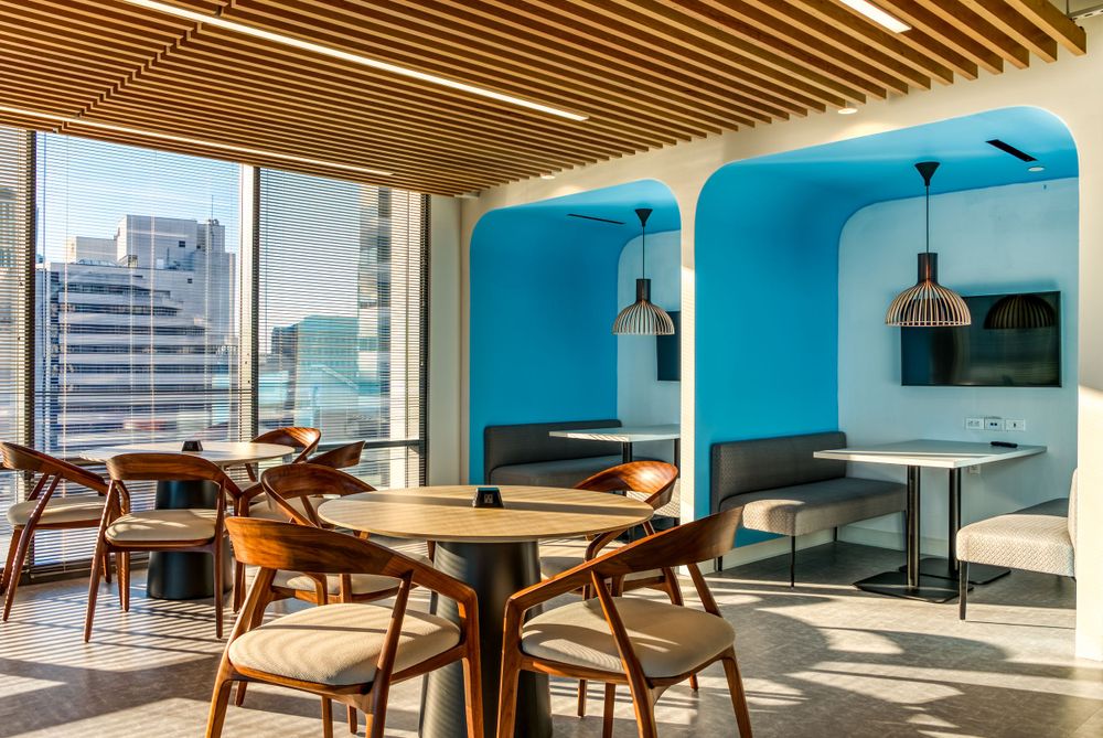 Modern dining space with curved blue accent walls, wooden furniture and city views through floor-to-ceiling windows.