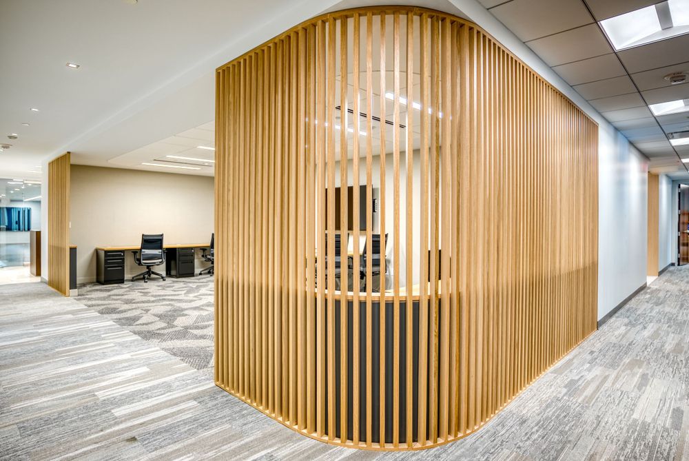 Office hallway with curved wooden slat wall design and gray carpeted flooring.