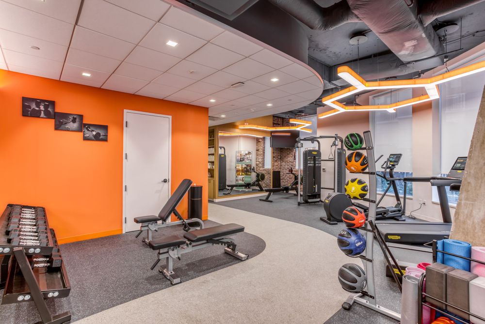 Fitness center with orange walls featuring cardio equipment and weight training machines.