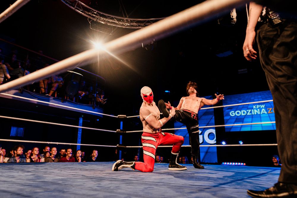 Two wrestlers engage in combat moves inside a blue-lit professional wrestling ring.