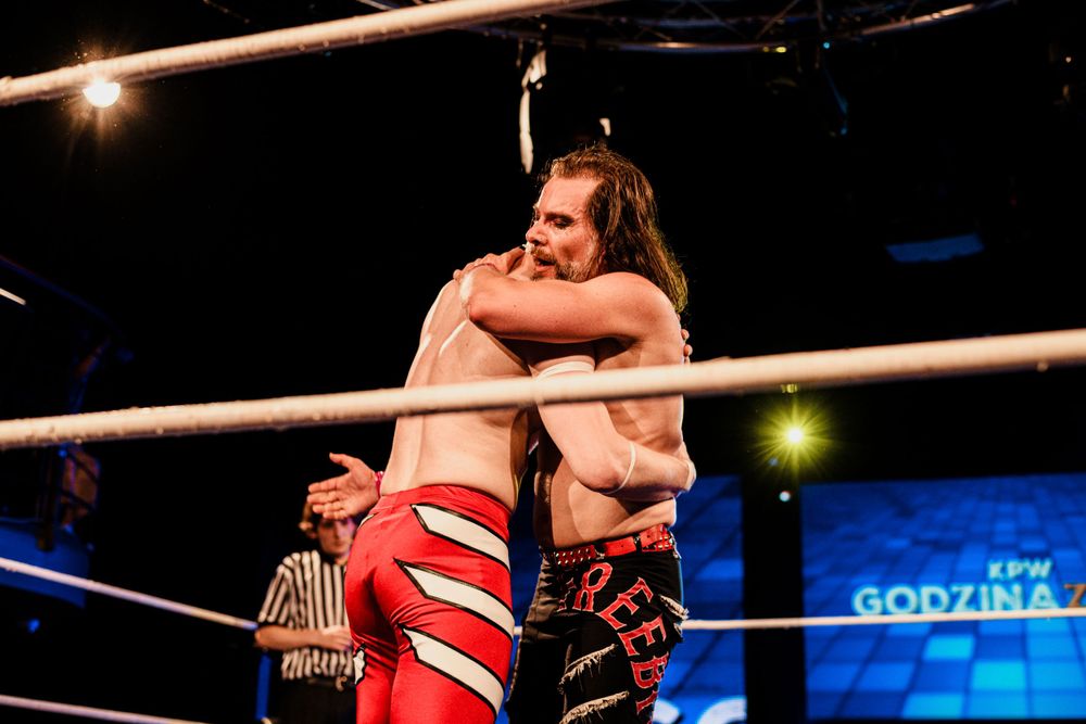Professional wrestlers celebrate after an intense match in a WWE style wrestling ring.