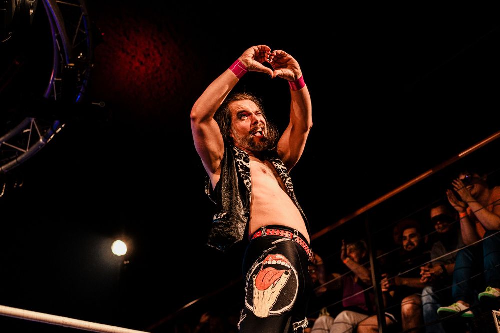 A wrestler makes a heart gesture with their hands while standing in the ring during a match.