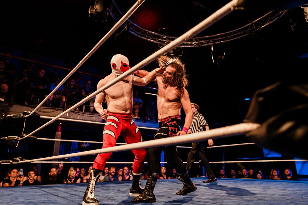 Two wrestlers locked in combat near the ropes during an intense match.