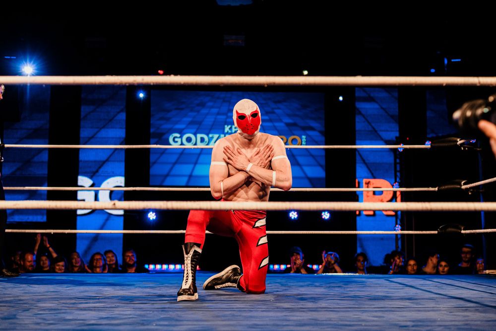 Wrestlers celebrate with raised arms in a wrestling ring during a nighttime event.
