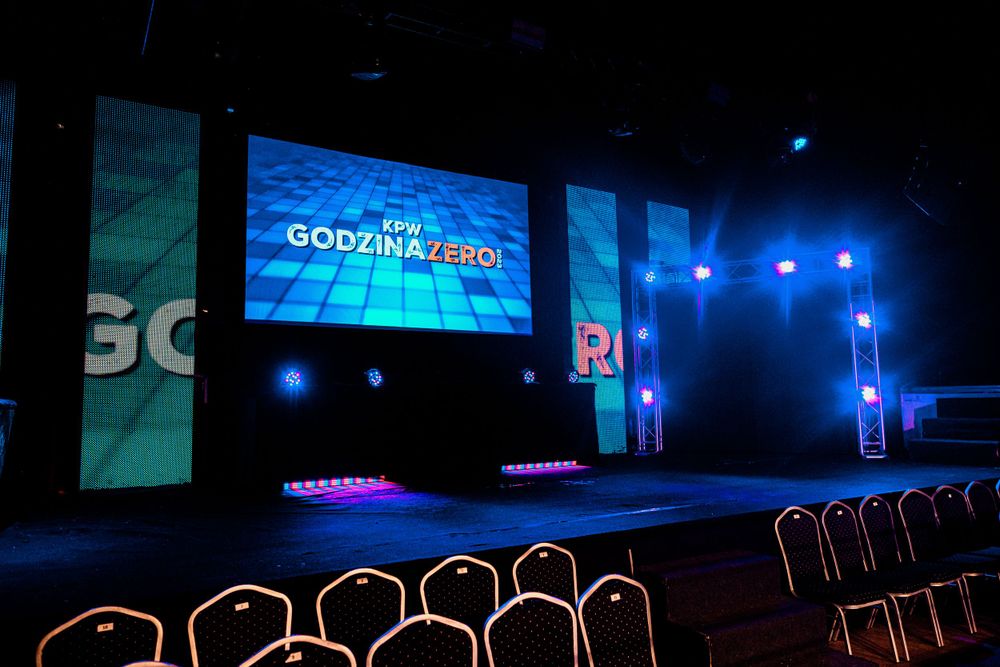 Empty chairs face a stage with blue lighting and a digital screen displaying 'Godzmilla Pro' text.