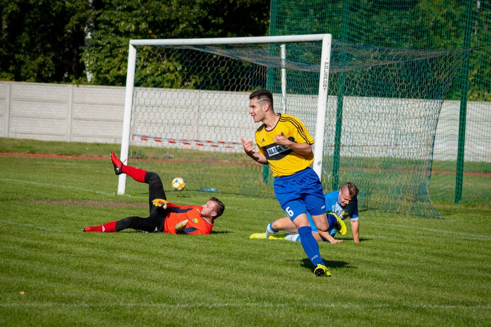 Soccer goalkeeper in yellow uniform defends the goal during a match on grass field.