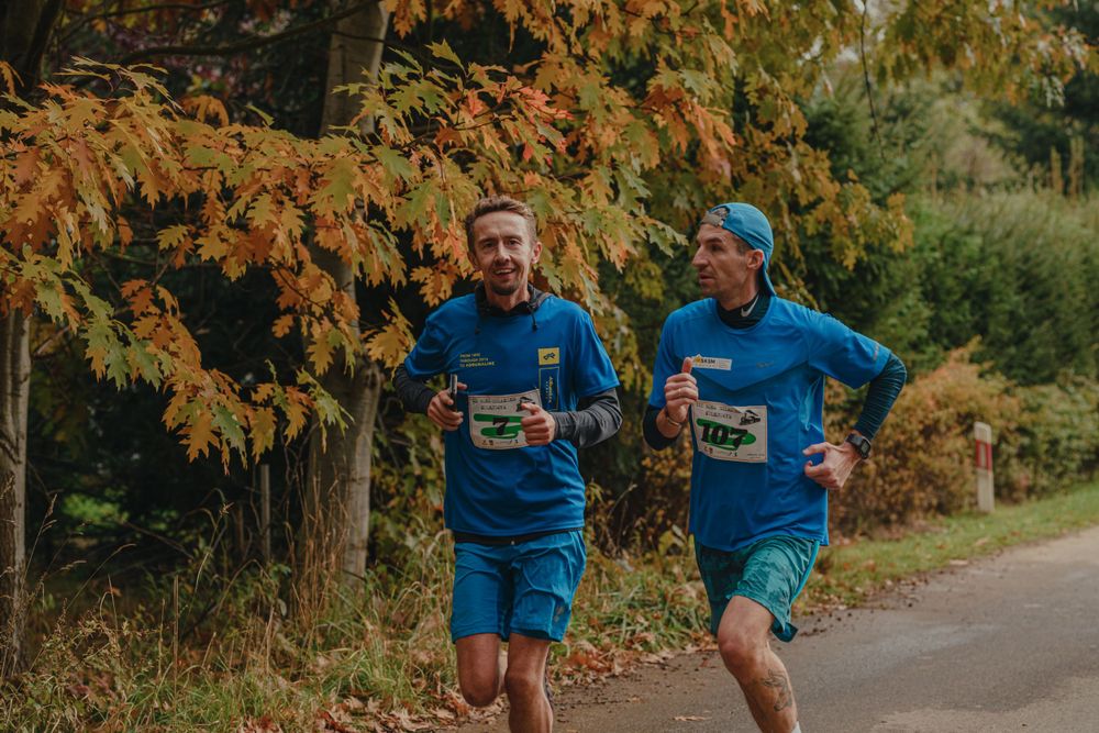 Athletes in blue uniforms running through a park with fall foliage.